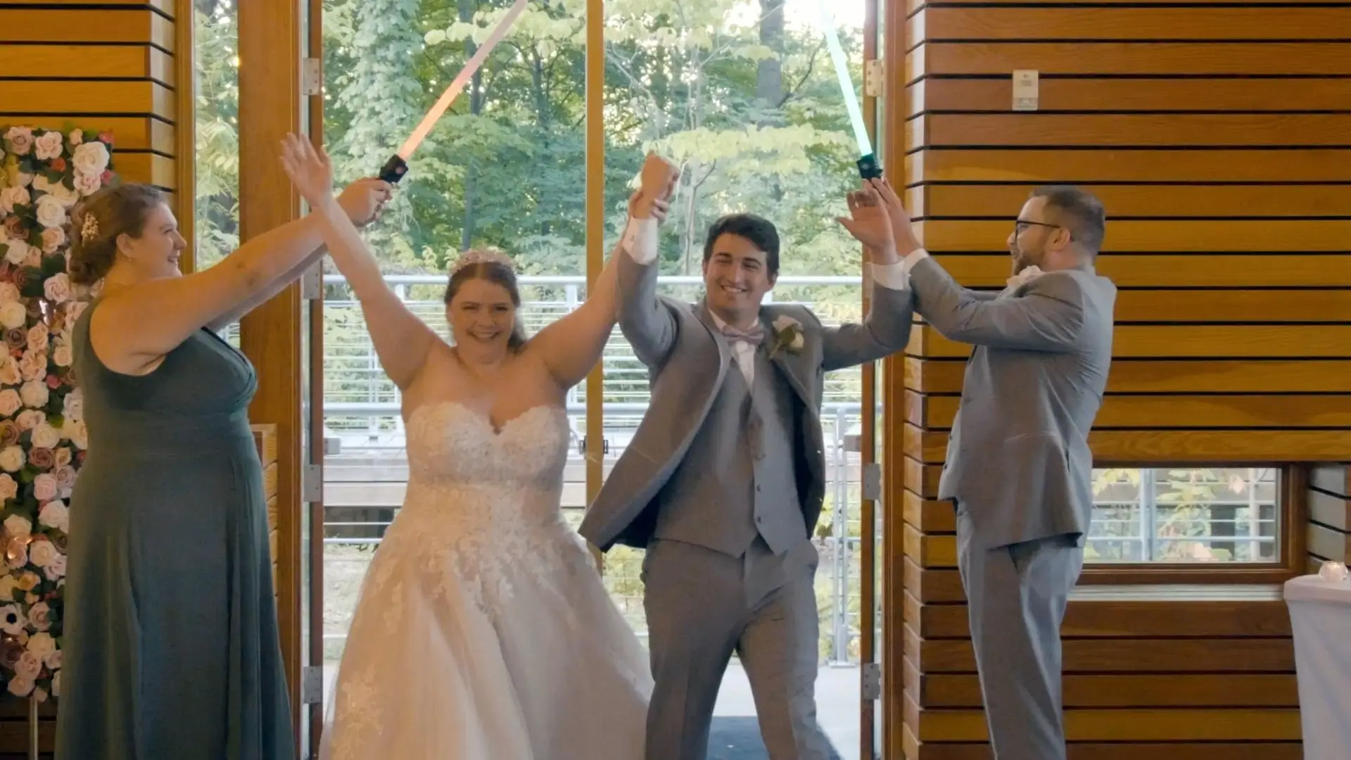 This still from Alexis and Carly's wedding video captures their first kiss as a married couple under a decorated arch, with the officiant smiling in the background. The scene is set outdoors in Traverse City, Michigan, surrounded by autumn leaves.