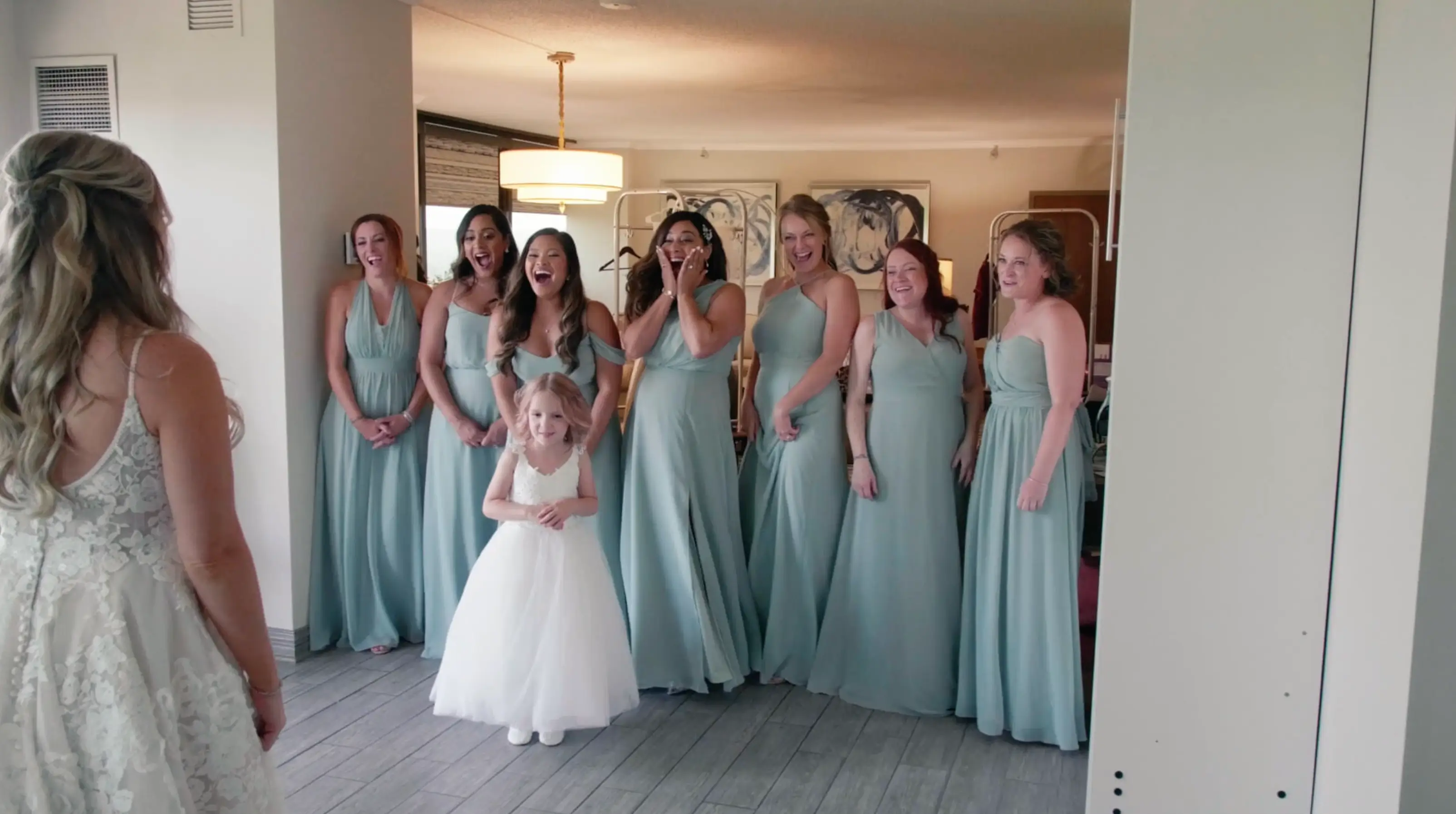 In this still from their wedding video, bride Nicole faces her bridesmaids and flower girl, all in light blue dresses, who react with joy in their suite at the Grand Traverse Resort & Spa in Traverse City.