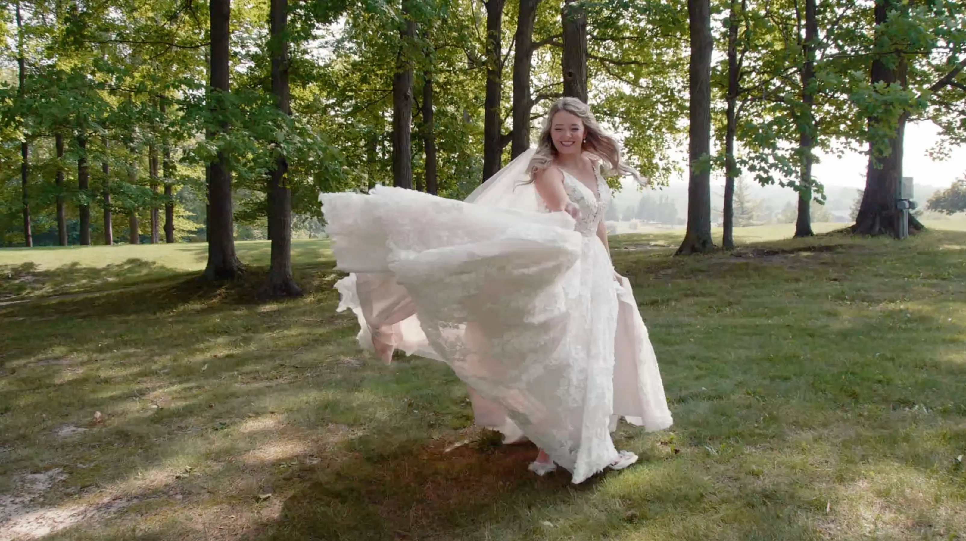 Bride Nicole twirling joyfully in her wedding dress in a serene, tree-lined area admist the lush, vibrant greenery of northern Michigan.