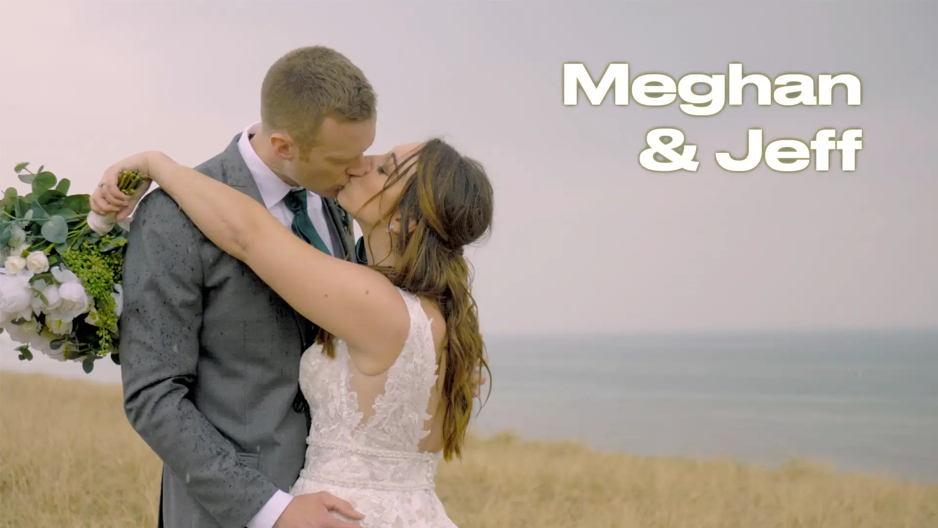 A wedding photo of Meghan and Jeff kissing in a field with a bouquet of flowers, near the ocean. Text on the image reads "Meghan & Jeff." Meghan is in a white lace wedding dress, and Jeff is in a gray suit with a tie.