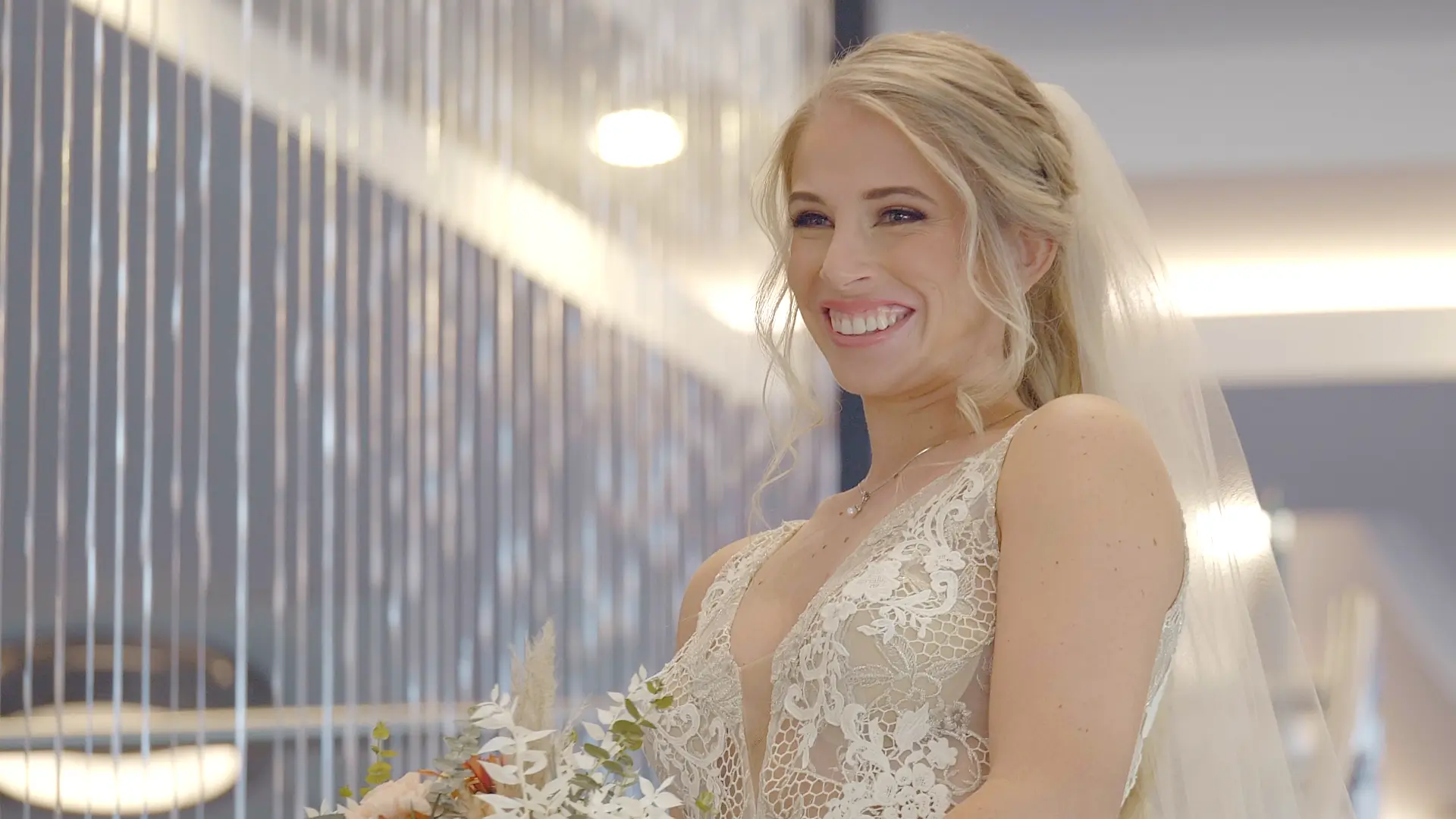 Dana smiles brightly in her lace wedding dress and veil, holding a bouquet during her Fall wedding in Michigan.