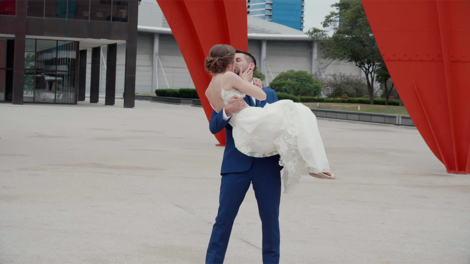 In this still from their wedding video in Grand Rapids, Kathryn and Esteban share a romantic kiss as Esteban lifts Kathryn in his arms against a backdrop of the Calder Plaza, captured by their wedding videographer.