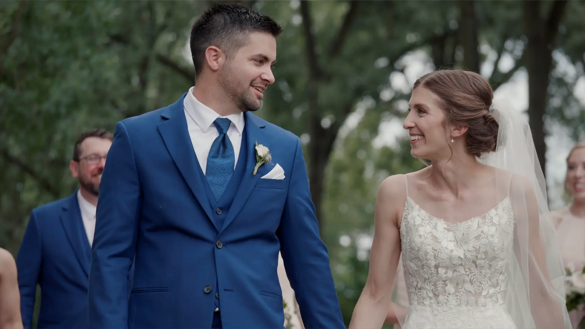 Kathryn and Esteban smile at each other while holding hands on their wedding day in Downtown Grand Rapids. Kathryn wears a white lace gown with a veil, and Esteban is in a blue suit with a white boutonniere.