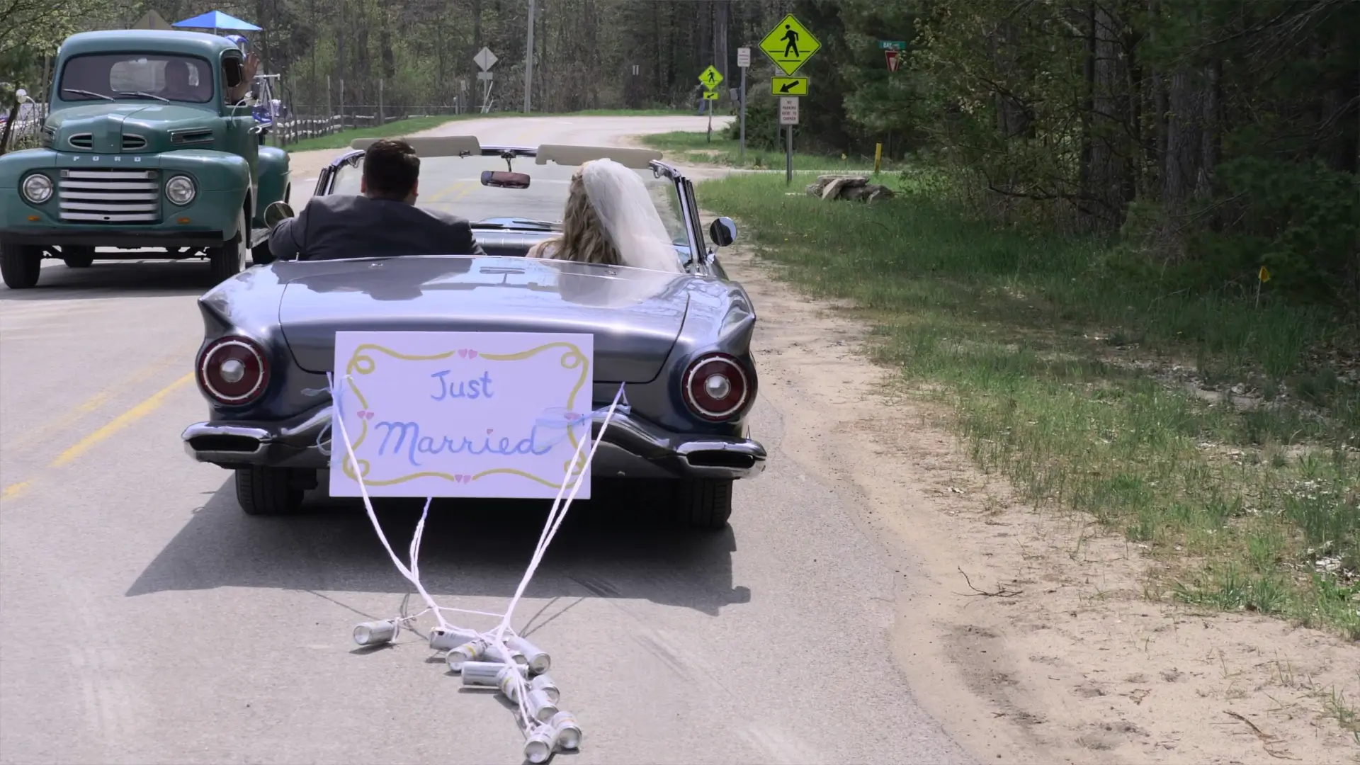 Amanda and Clark's "Just Married" car drives away through lush Michigan greenery, with cans tied to the back and a retro truck nearby.