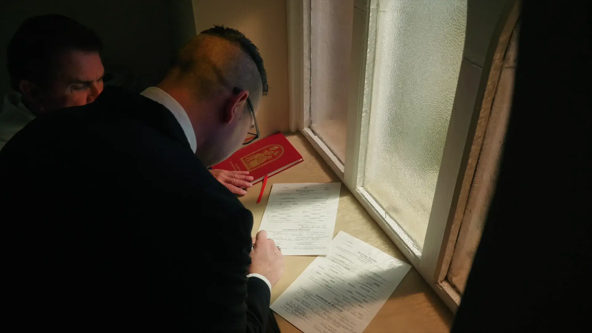 In this snapshot from their wedding, groom Leigh signs their marriage license by a window at St. Augustine's Catholic Church in Howell, Michigan.