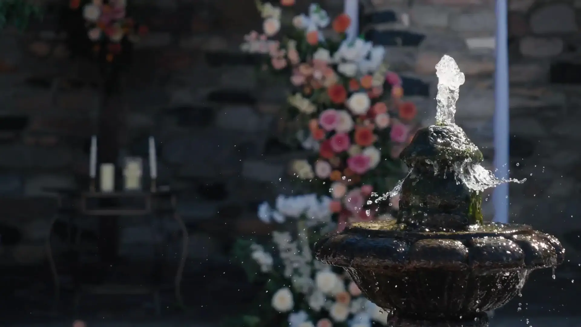 A stone fountain splashes water elegantly in the foreground, with colorful floral arrangements creating a romantic backdrop. The scene captures the essence of an outdoor wedding setting at Castle Farms in Michigan.
