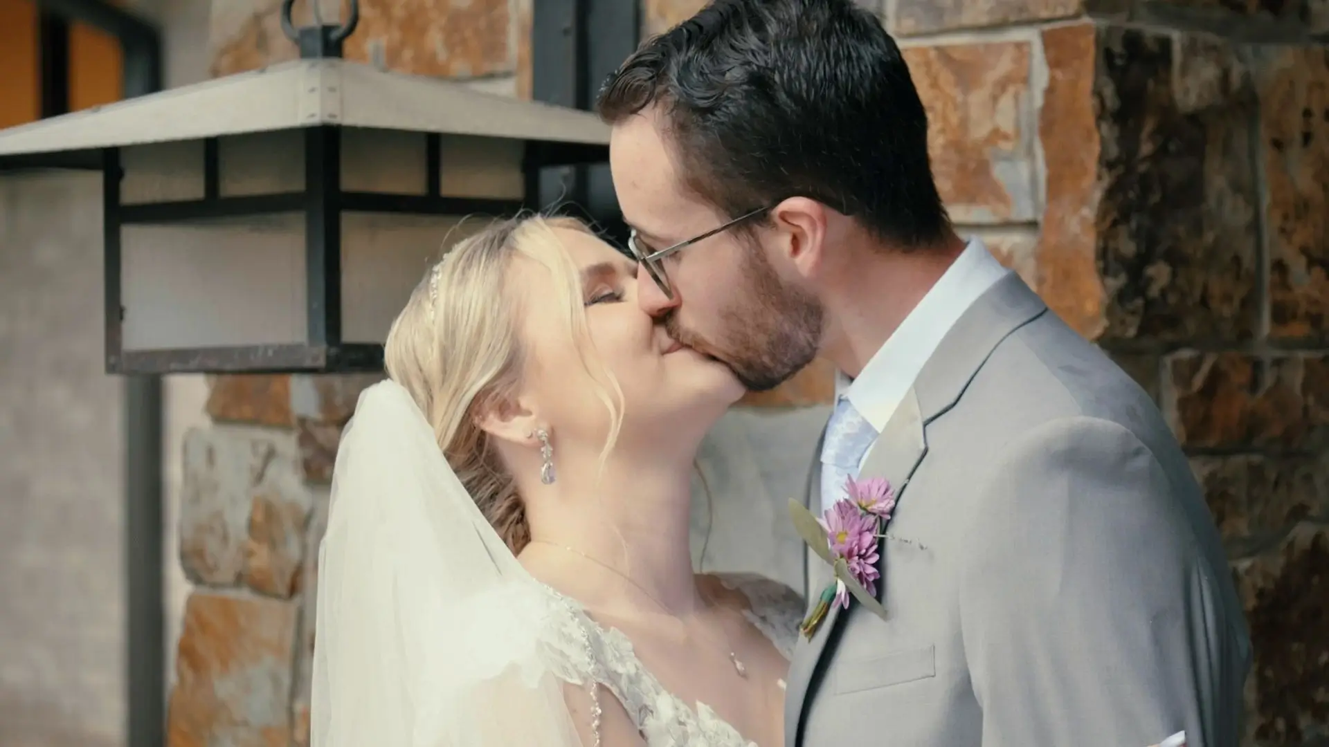 Bride and groom, McKenna and Jacob, share a kiss during their wedding at The Union Pavilion at Railside. The bride, wearing a lace gown and veil, and the groom, in a gray suit with a flower boutonnière, are captured in a romantic moment.