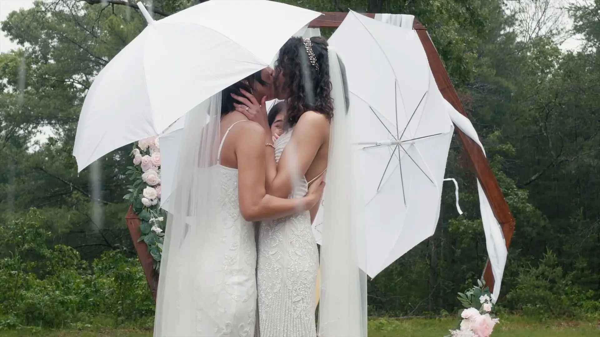 In this emotional snapshot from their wedding video, Irene and Claudia share a kiss under white umbrellas during their outdoor ceremony in Newaygo. The scene is intimate and heartfelt, captured beautifully despite the rainy Michigan weather.