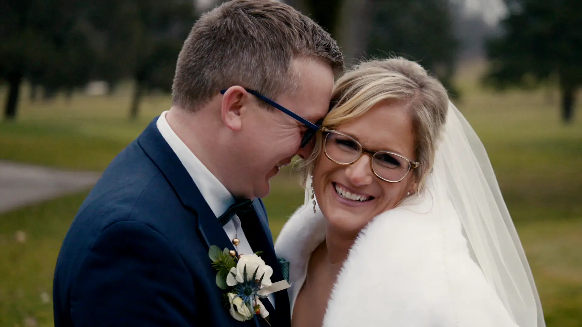 Bride and groom smiling warmly, embracing against a backdrop of serene Michigan greenery on their wedding day.