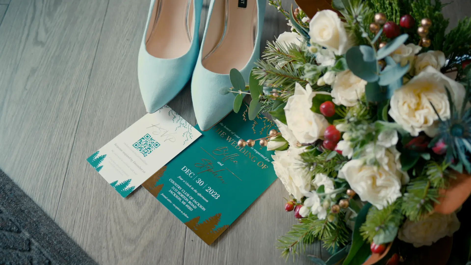 Wedding invitation and RSVP card for Billie and Stephen's December 30, 2023 wedding at Country Club of Jackson, displayed with light blue heels and a bouquet of white and red flowers on a wooden floor.
