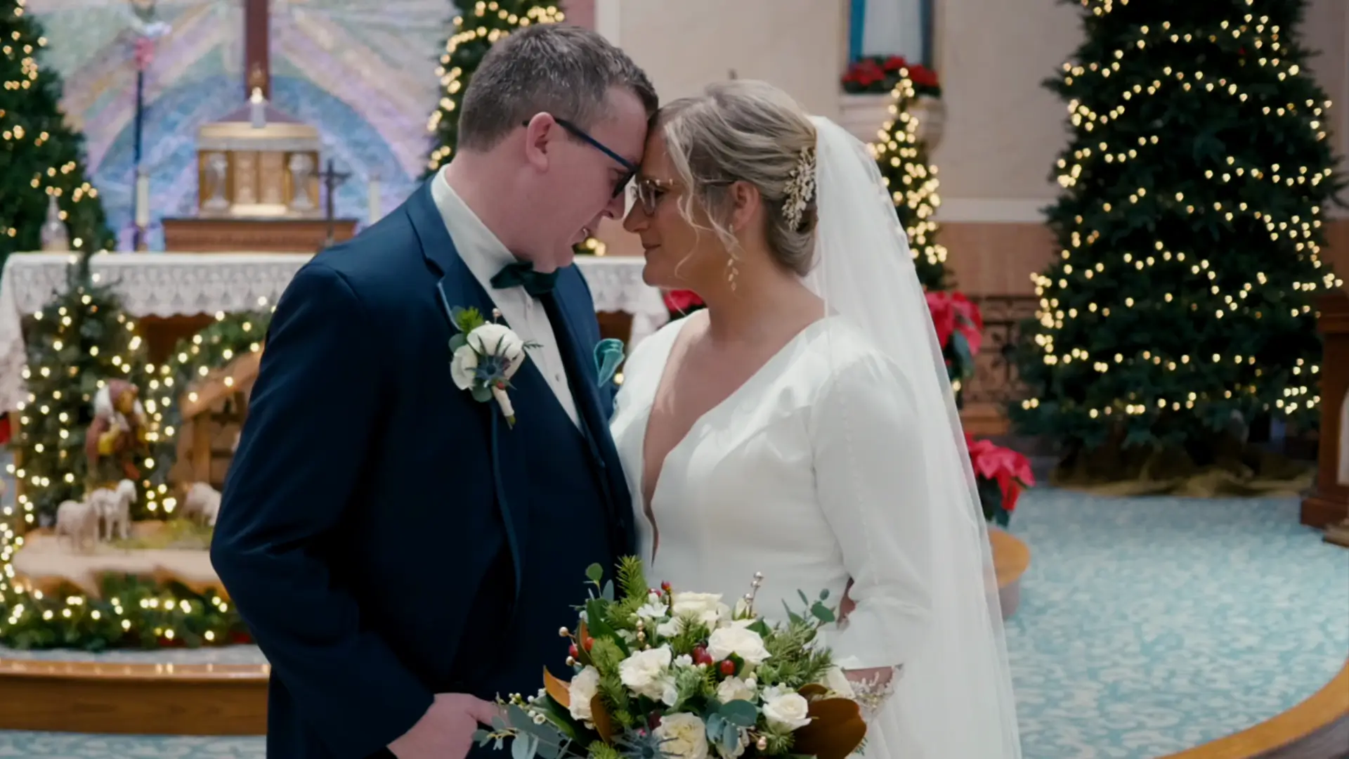 Billie and Stephen share a tender moment at Queen of the Miraculous Medal Church in Jackson, captured in this wedding video still. Surrounded by festive decor, the couple stands head-to-head, holding a bouquet, celebrating their special day in Michigan.