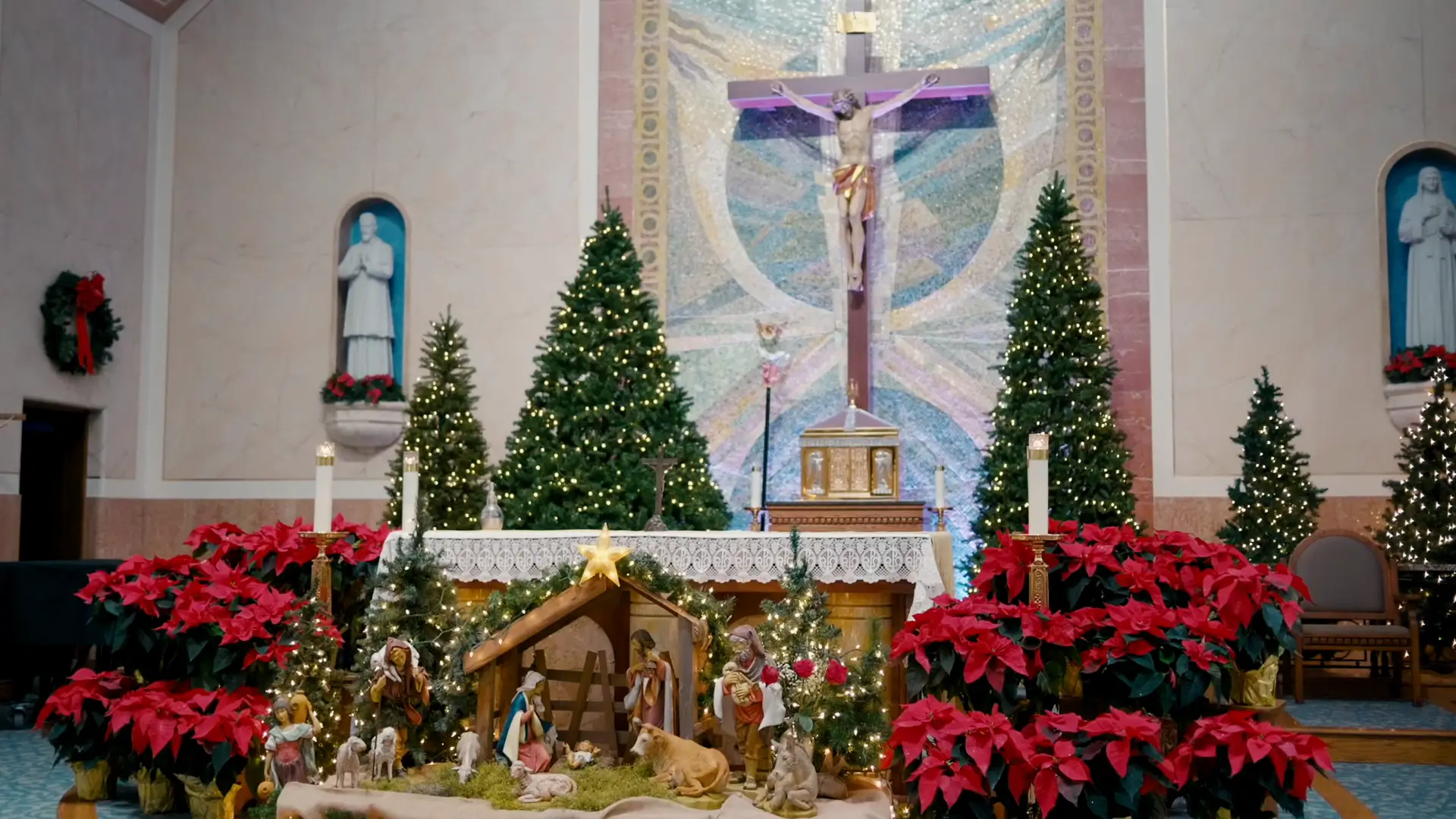 The church altar at Queen of the Miraculous Medal is beautifully adorned with a nativity scene, poinsettias, Christmas trees, and statues, captured elegantly by the wedding videographer for Billie and Stephen's ceremony in Jackson, Michigan.