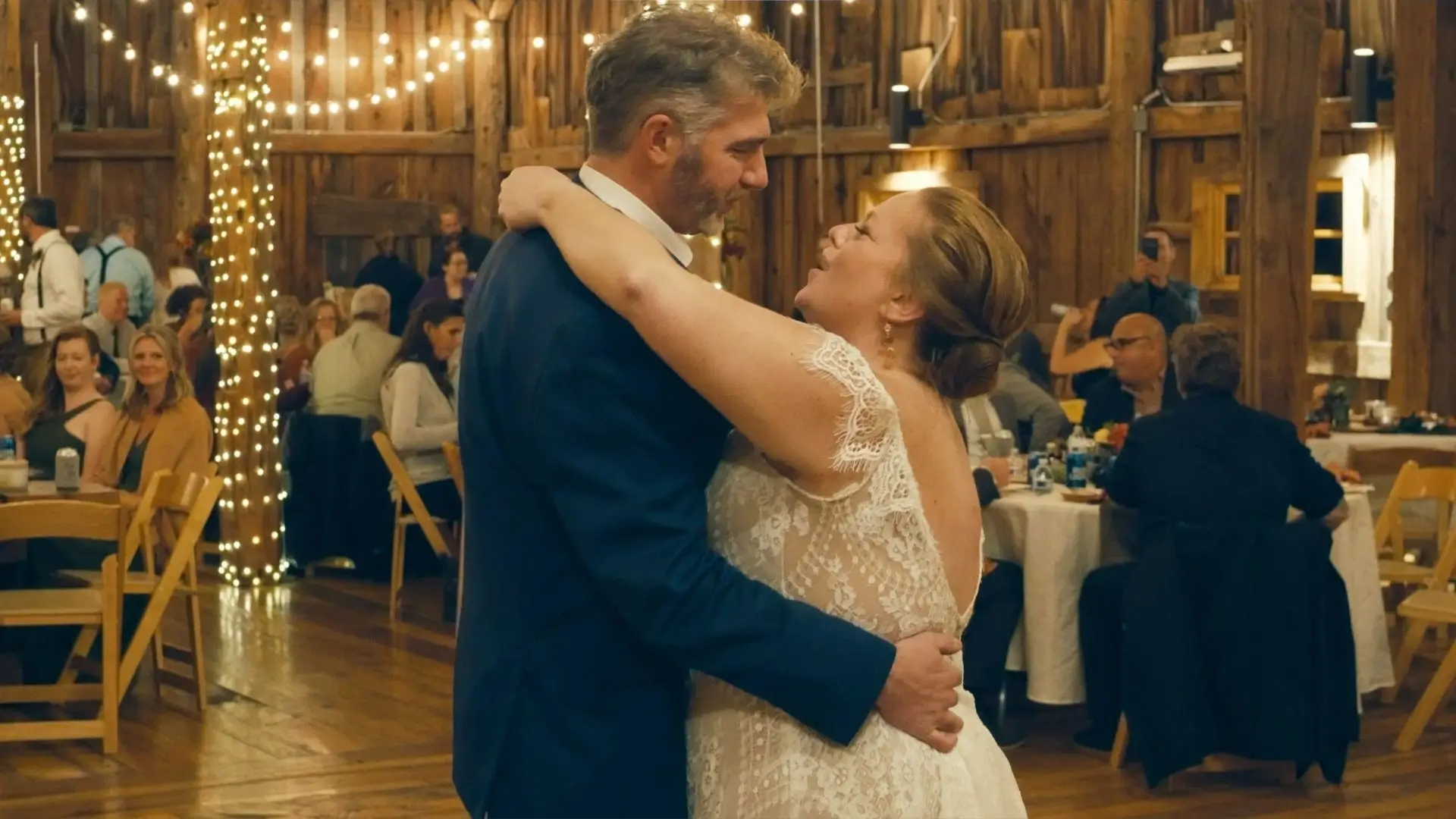 In this still from their wedding in Suttons Bay, Michigan, Beth and Aaron share a romantic first dance as their guests look on. String lights and rustic decor enhance the festive atmosphere captured by their videographer.