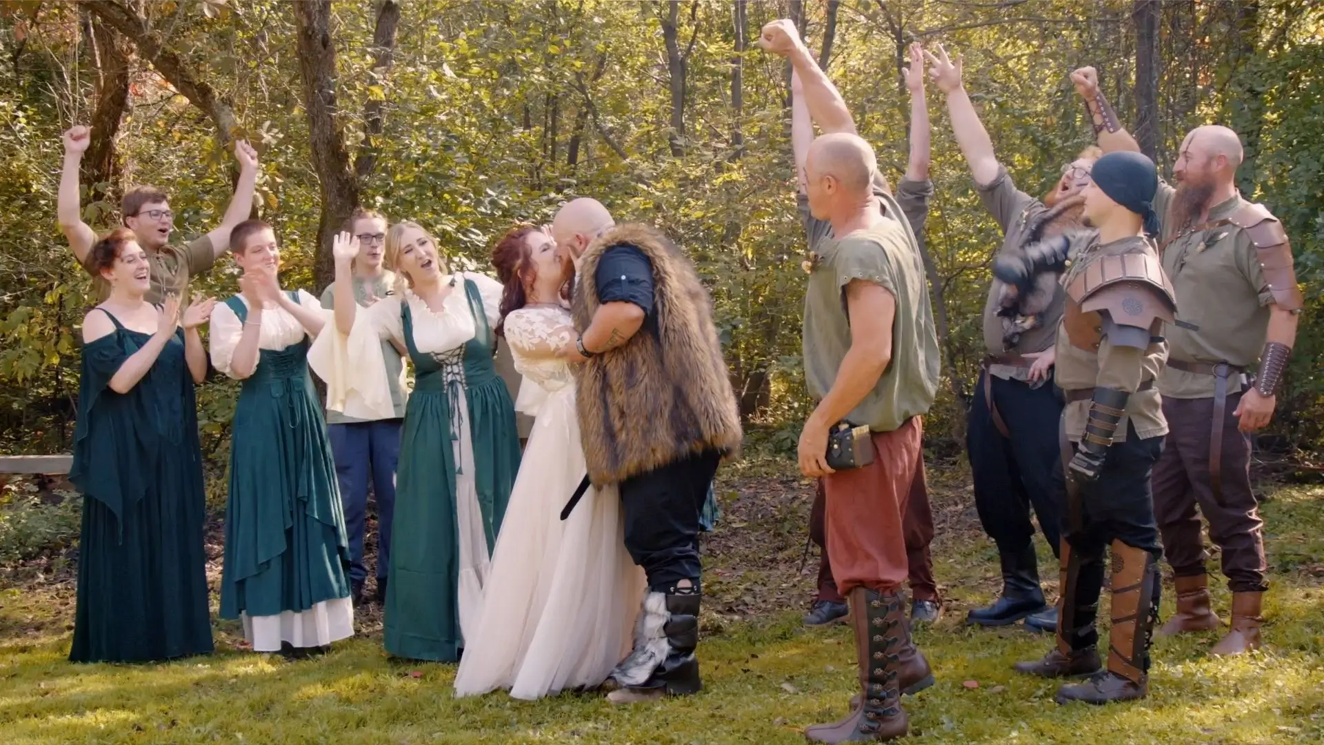 In this still from their wedding video, Milah and Keith share a kiss during their Viking-themed backyard wedding ceremony. The wedding party, dressed in period costumes and warpaint, cheers and celebrates around them in this candid moment.