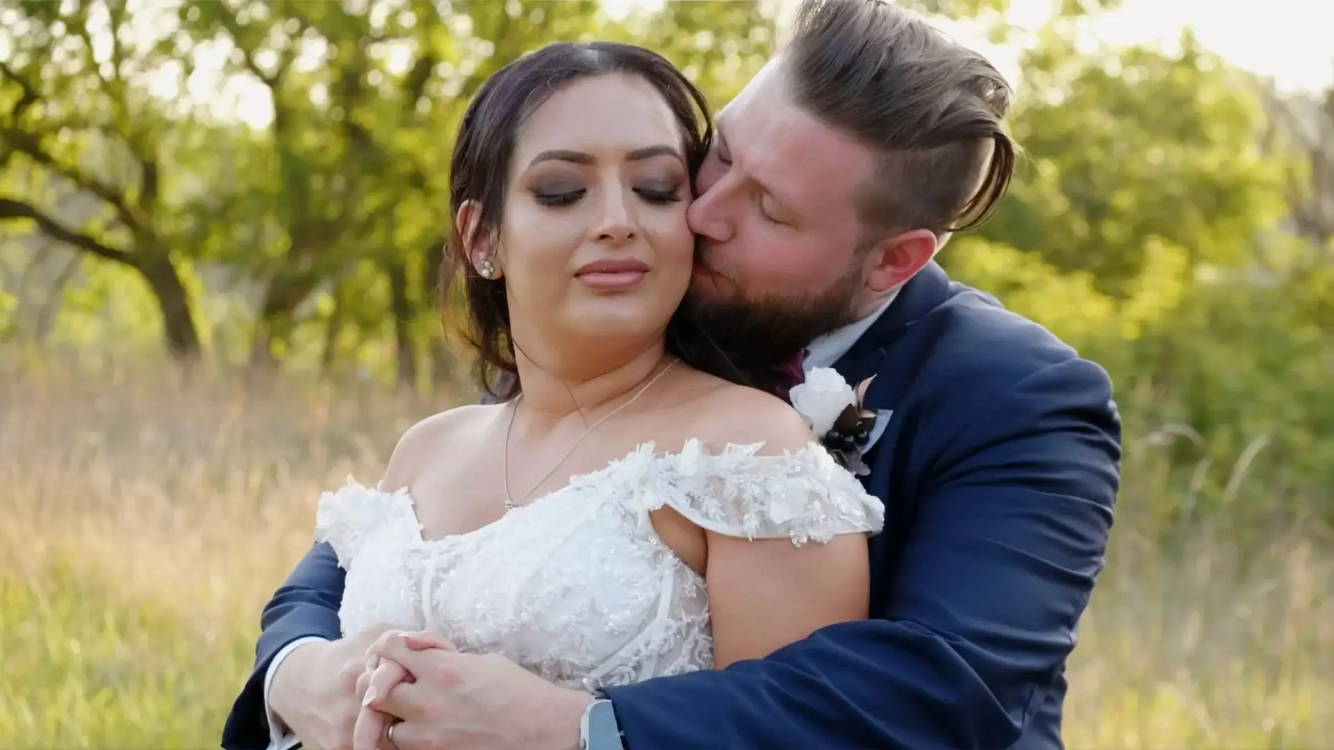 In this snapshot from their wedding highlight video, Yesenia and Thomas embrace tenderly in front of lush greenery at Something Blue Berry Farm, captured by their videographer.