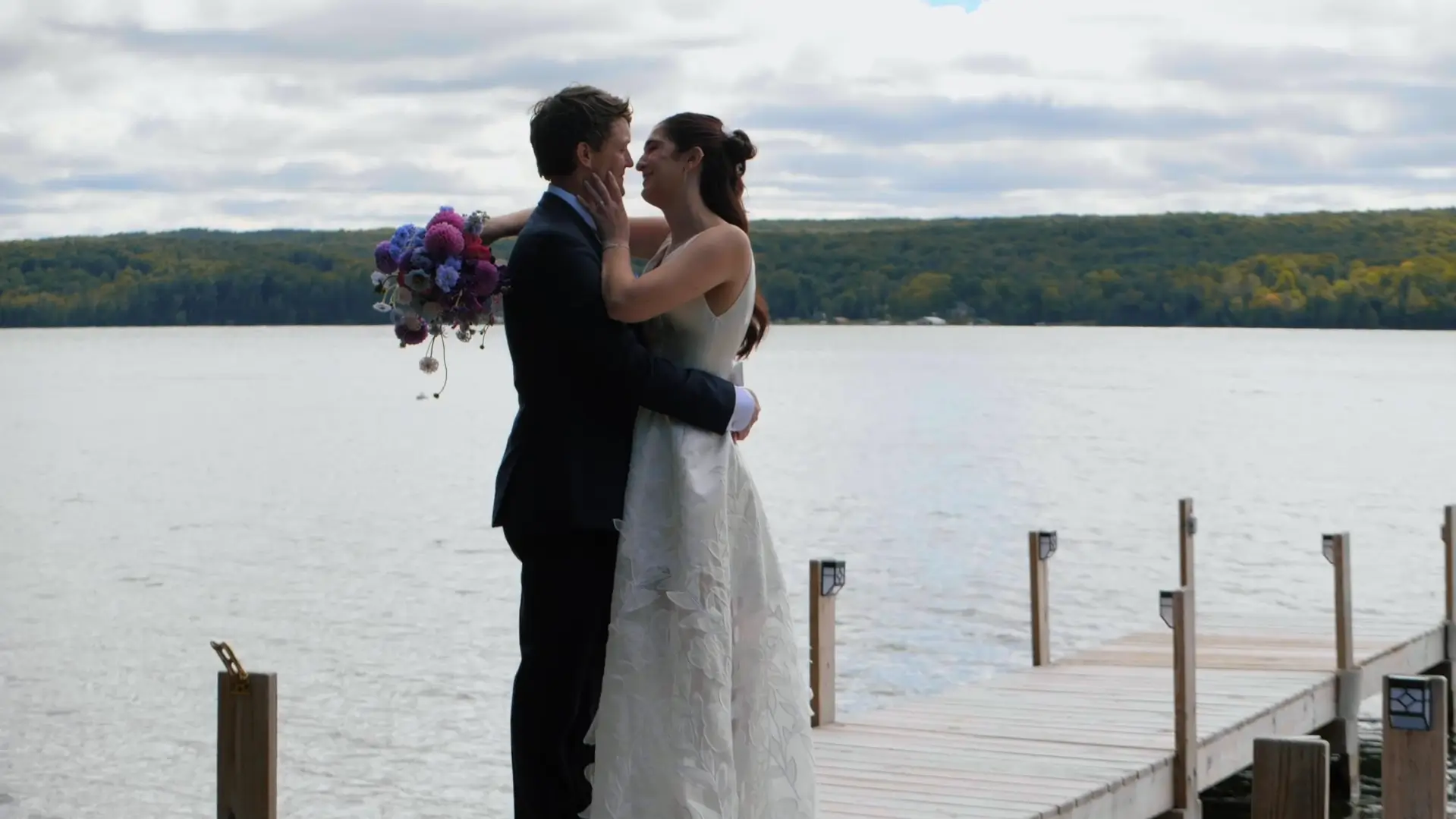 Bride and groom, Chloe and Joe, embrace on a dock by a beautiful Michigan waterfront, with lush greenery in the background, Chloe holding a vibrant bouquet.