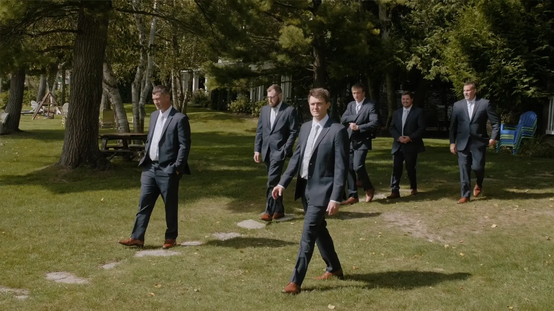 Groomsmen in dark suits walk through lush Michigan greenery at Chloe and Joe's wedding in Walloon Lake, Michigan.
