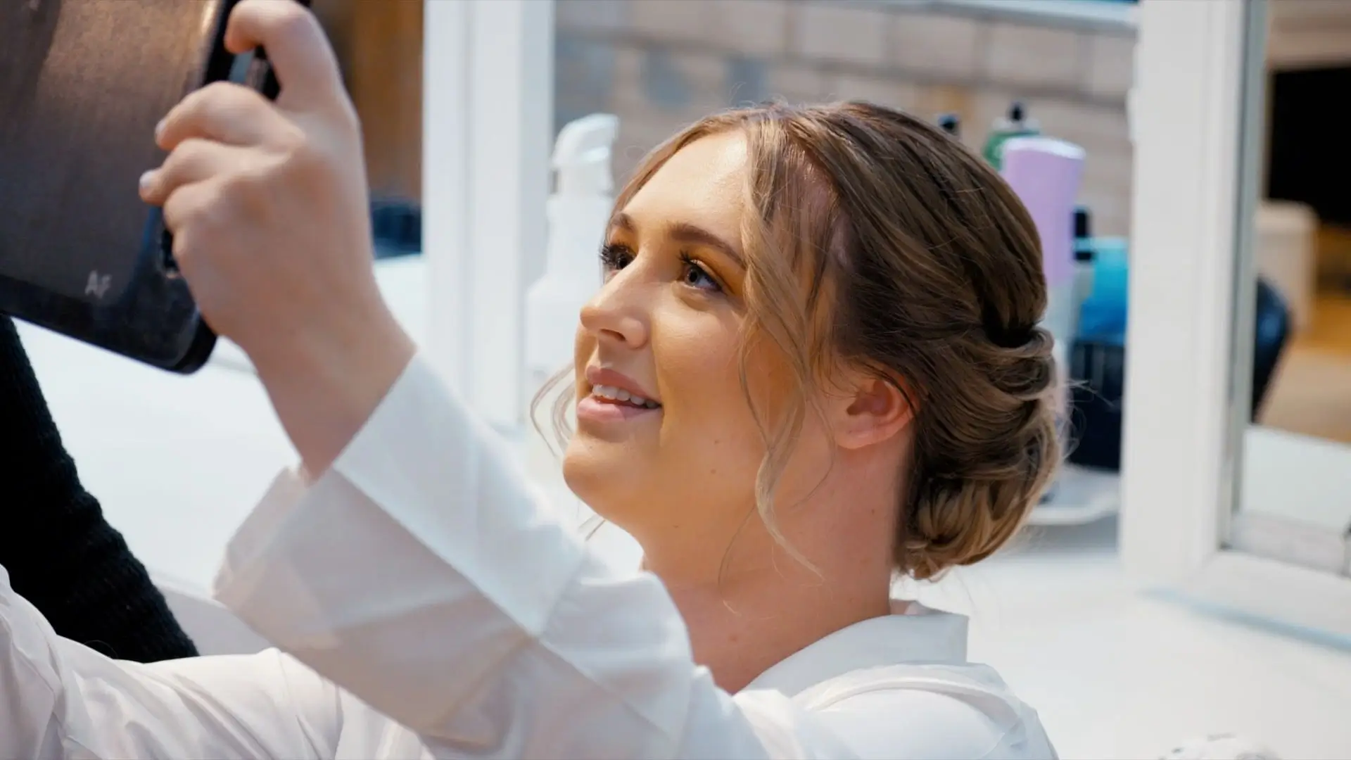 A close-up of bride Anna, smiling and adjusting her hair while looking into a handheld mirror, captured in a candid moment by the wedding videographer at her wedding in Holland.