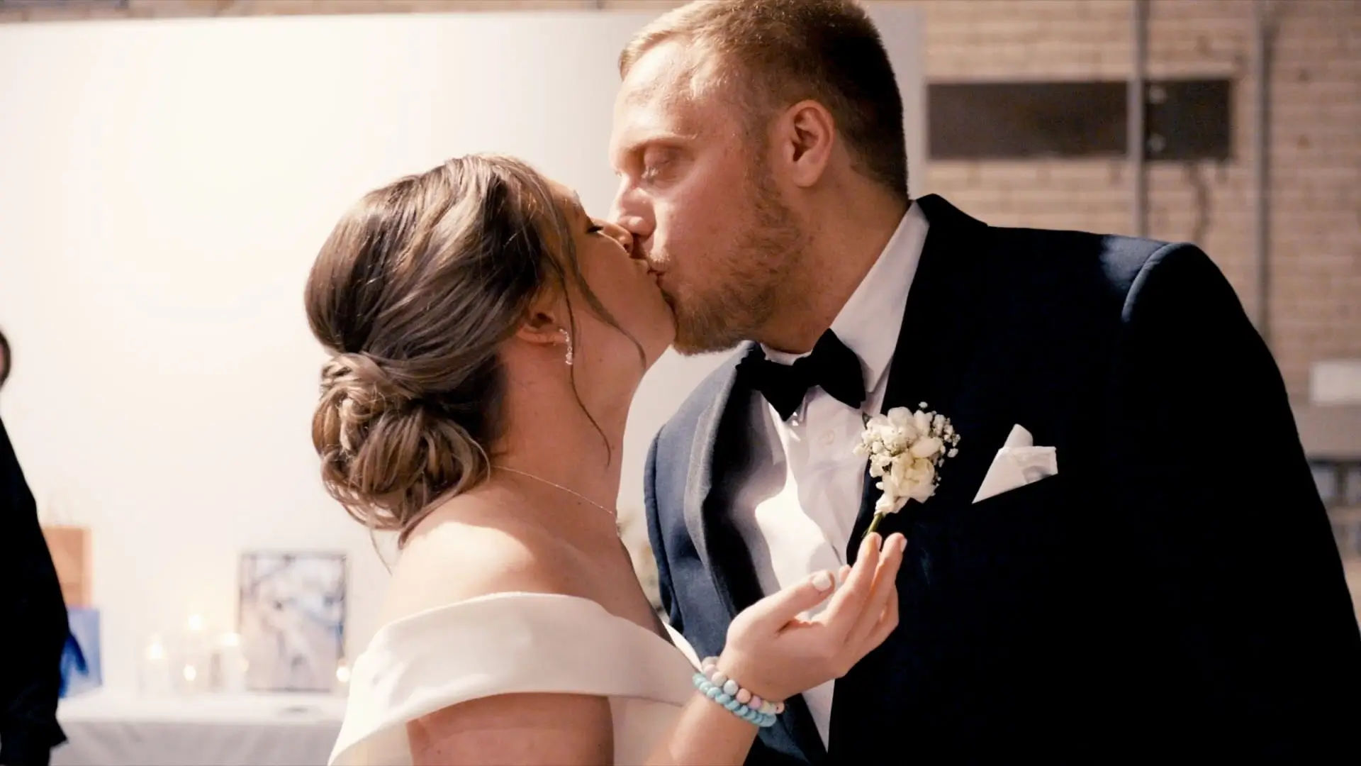 Anna and Kevin share a kiss on their wedding day at Baker Events in Holland. Anna is in an off-the-shoulder dress with her hair in an elegant bun, and Kevin is in a navy suit with a white boutonniere and bow tie.