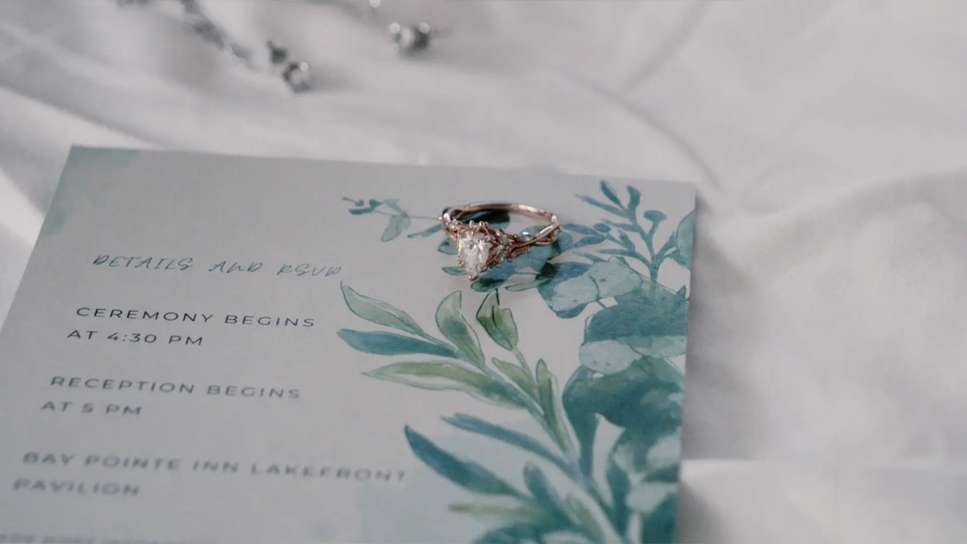 Wedding invitation with floral design and a ring placed on top. Details include ceremony and reception times.