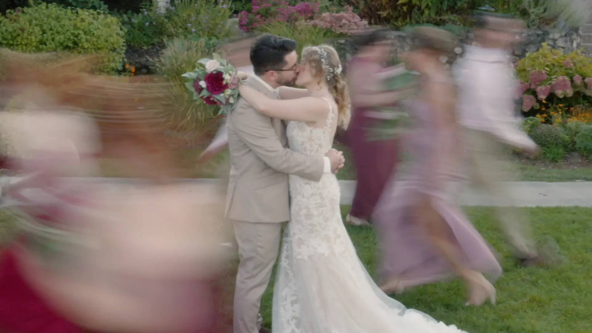 In this still from their wedding video, the bride and groom embrace and kiss amidst a blur of motion around them, captured by their wedding videographer.