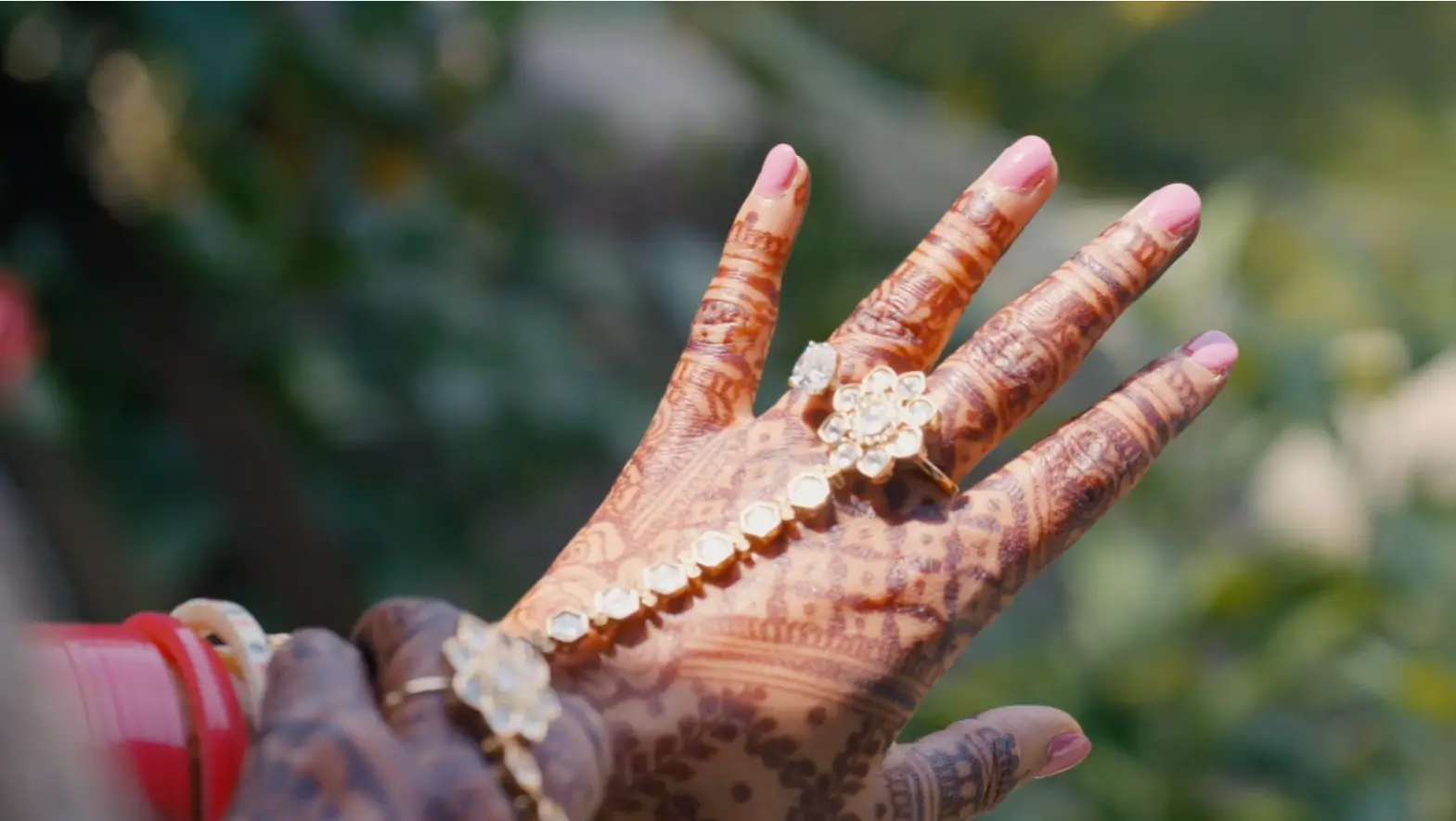 In this still from their wedding video, a hand adorned with intricate henna designs and elegant jewelry is captured, symbolizing a bride's preparation.