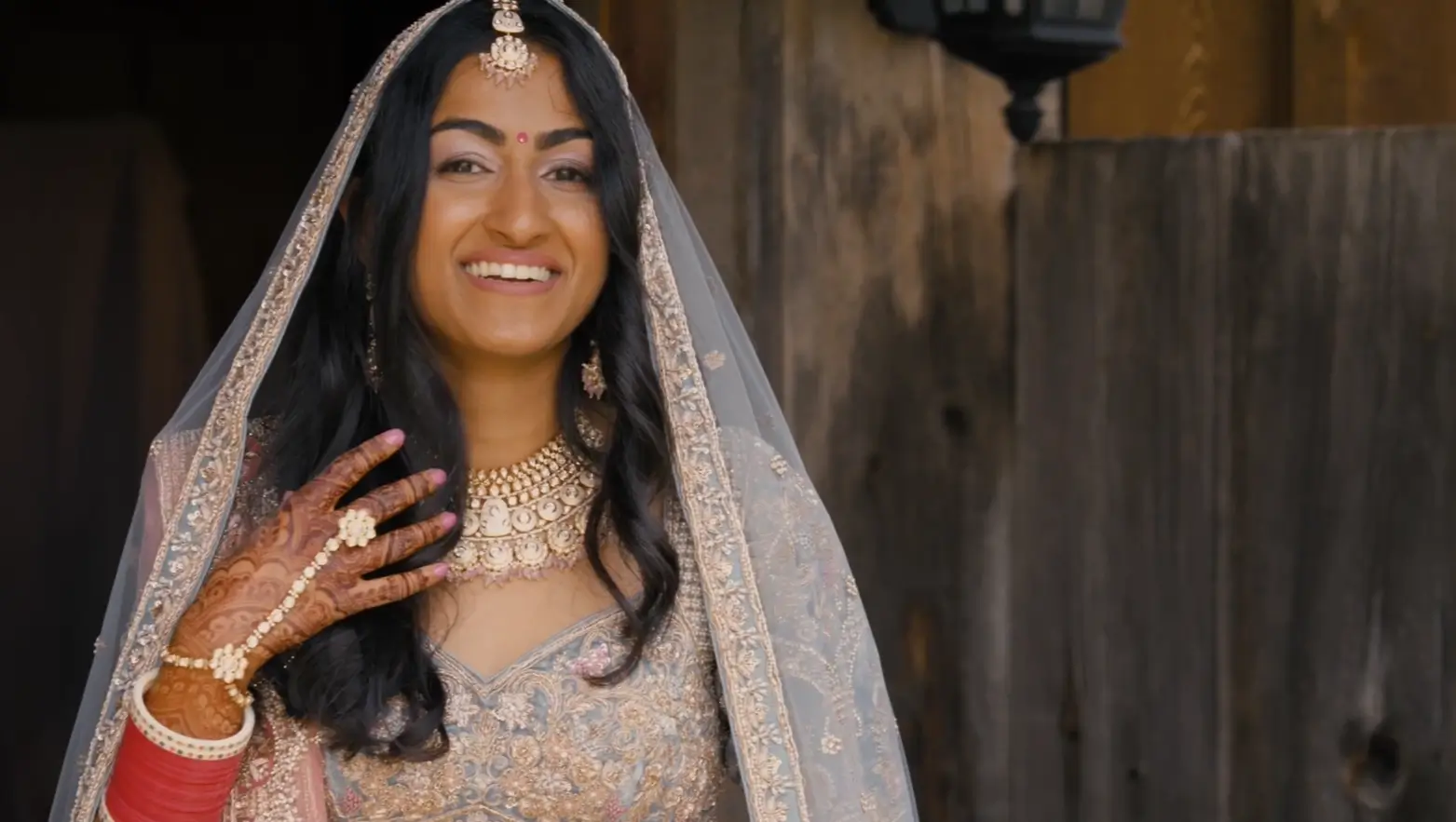 In this still from their wedding video, the bride is smiling while wearing an intricate traditional dress, captured by their wedding videographer.