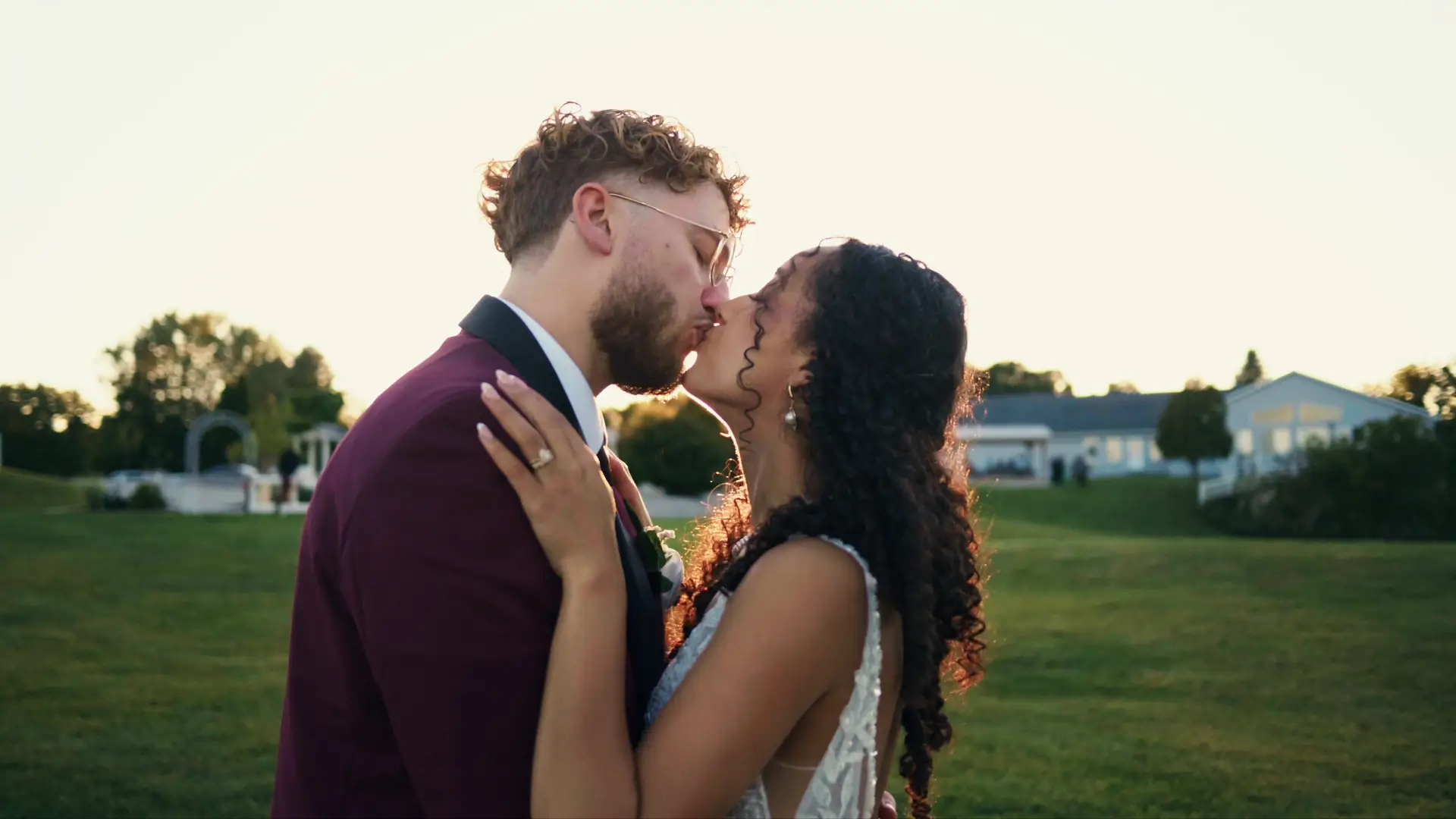 A romantic moment between a bride and groom, captured outdoors during sunset, as they share a kiss in this still from their wedding video.