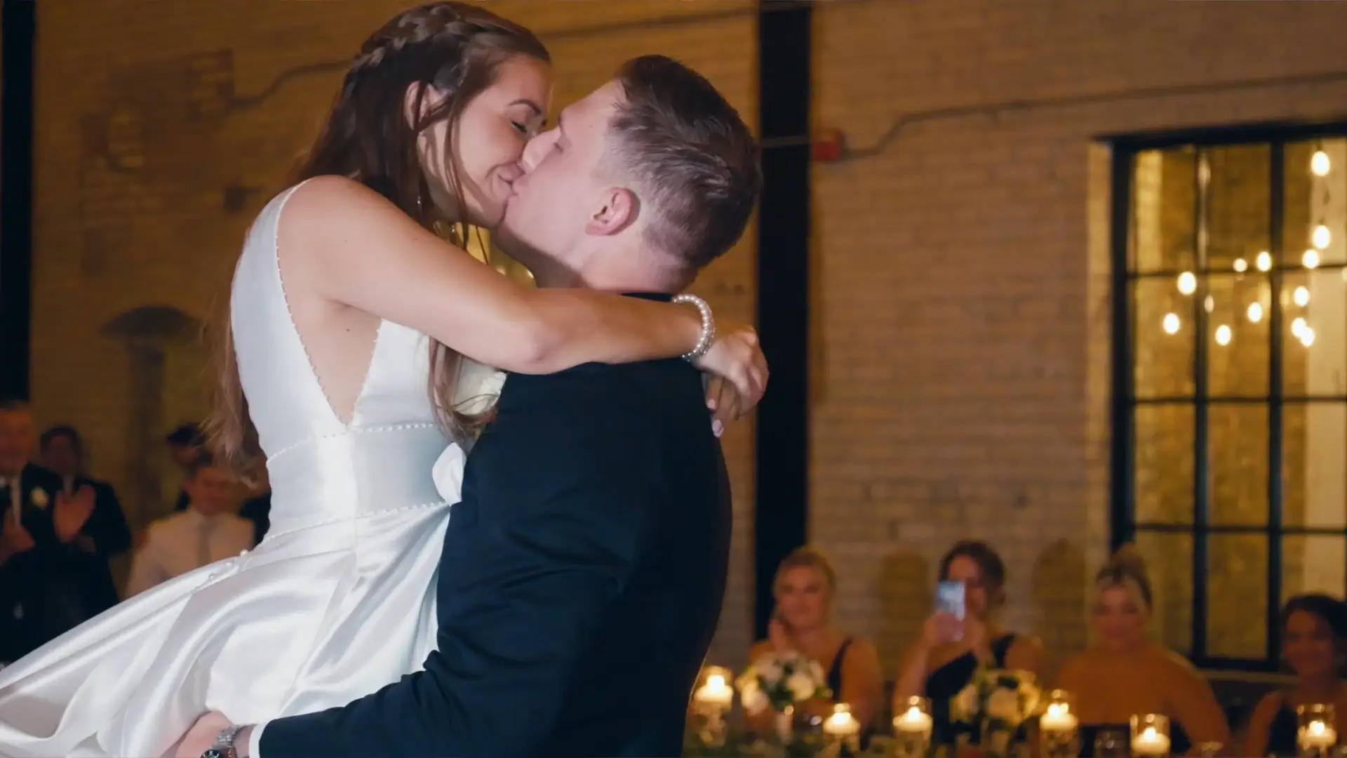 Madison and Max share a romantic kiss during their first dance at New Vintage Place, Grand Rapids, Michigan, captured by their wedding videographer. The warm lighting and intimate atmosphere highlight this cherished wedding moment.