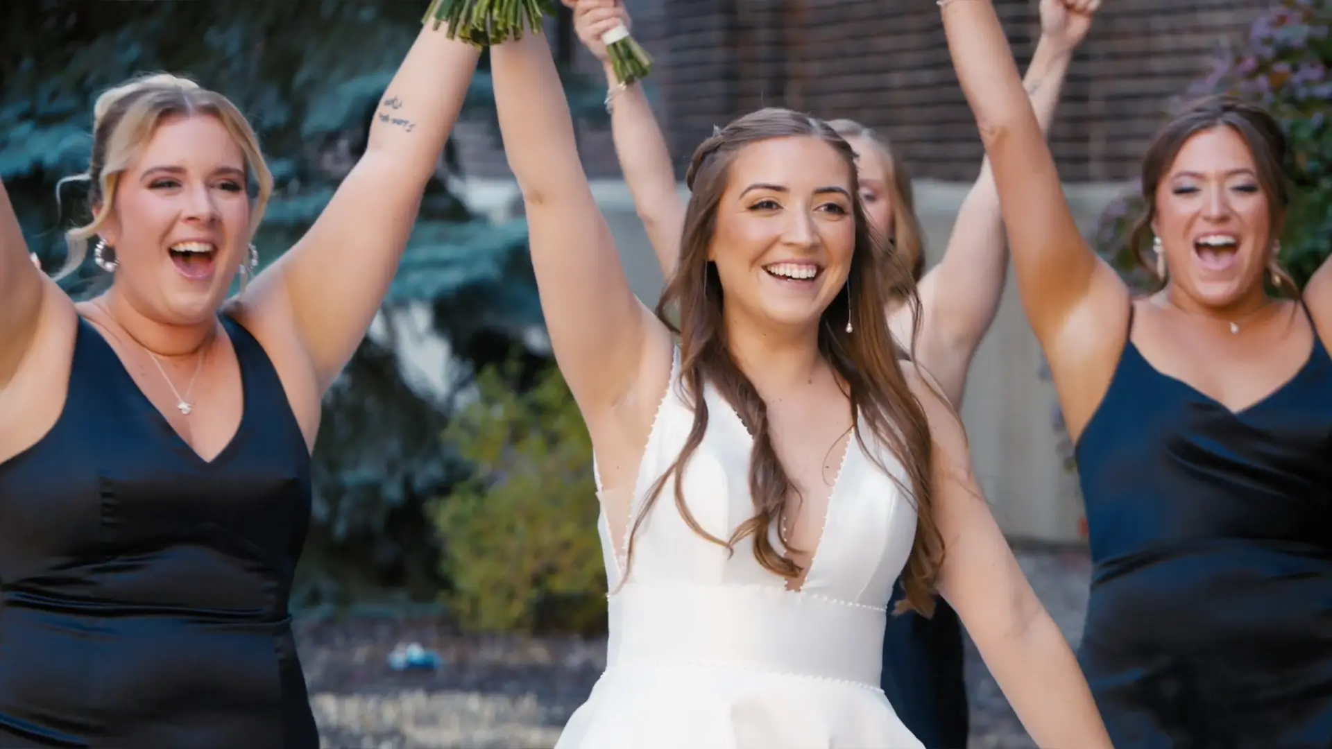 In this lively snapshot from her wedding videographer, Madison smiles joyfully alongside her bridal party, arms raised in celebration. The vibrant Michigan greenery in the background adds a stunning touch to their memorable day.