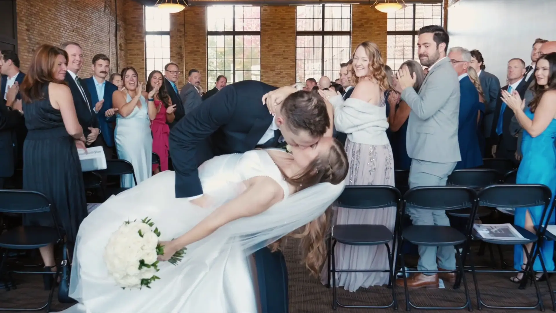 In this vibrant wedding highlight, Madison and Max share a romantic kiss as guests applaud around them, captured beautifully by their wedding videographer in Grand Rapids.