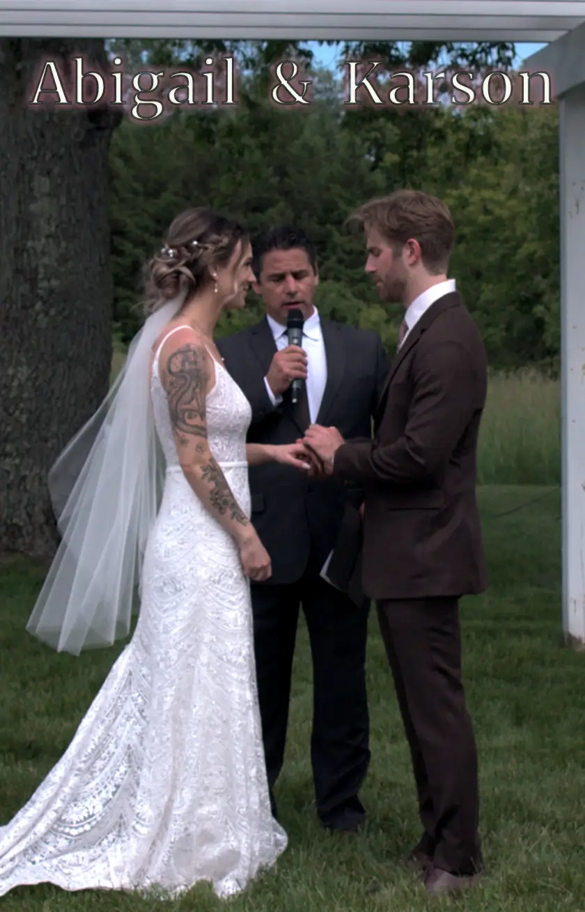 In this snapshot from their wedding videography at Hydrangea Blu Barn, Abigail and Karson exchange vows amidst lush Michigan greenery. The couple stands hand in hand with the officiant between them, creating a heartfelt and intimate moment.