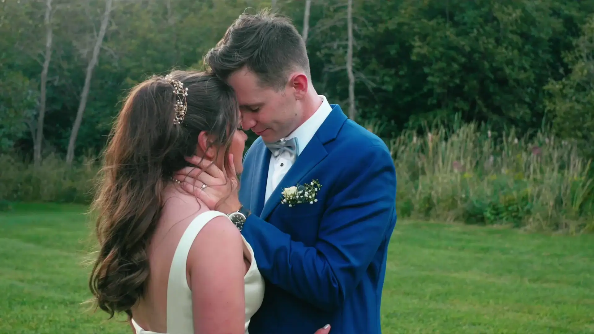 In this still from their wedding video, a bride and groom share an intimate moment outdoors, with the groom gently holding the bride's face, captured by their wedding videographer.