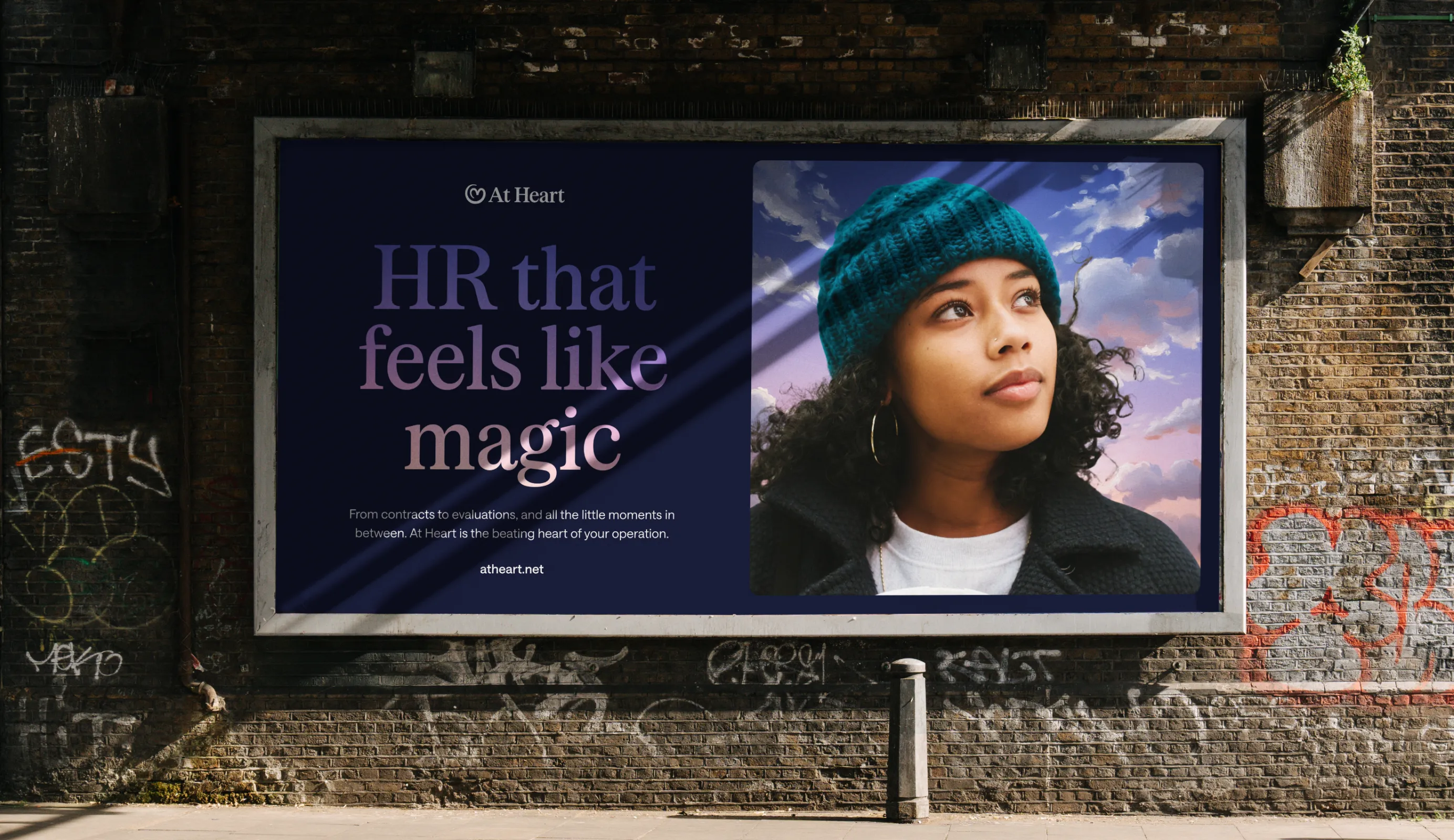 Billboard for At Heart showing the tagline 'HR that feels like magic' alongside the brand logo, a product notification and a portrait photo set against a painterly cloud sky.