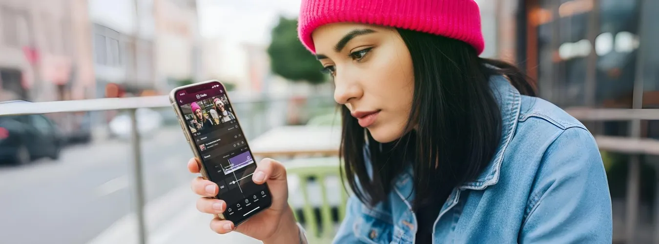 Mulher com gorro rosa edita vídeo em celular ao ar livre