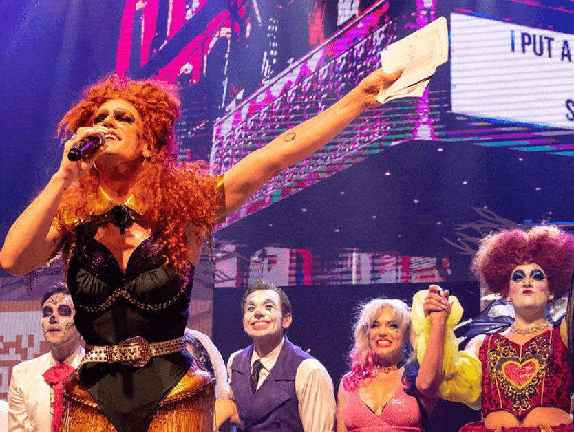 An image of performers presenting, smiling and gesturing to the side.