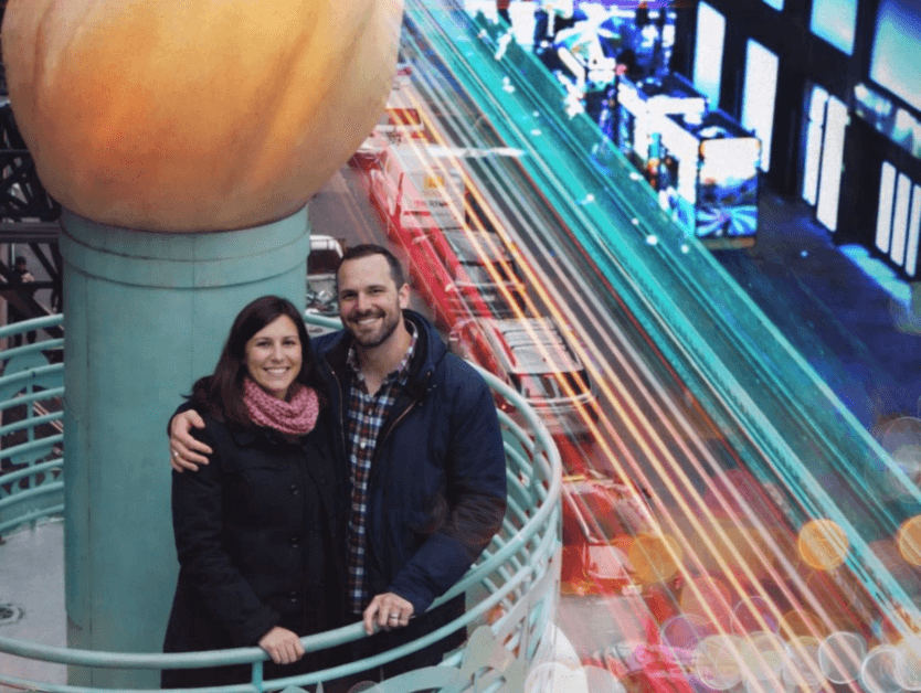 A couple standing together and smiling for a photo at the top of the torch at RiseNY