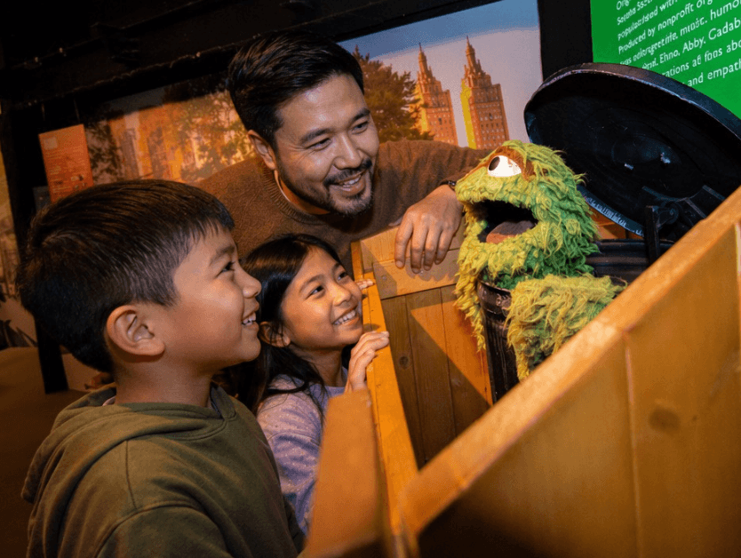 A family interacting with an Oscar the Grouch exhibit at RiseNY