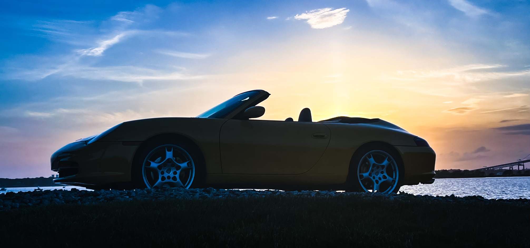 Porsche convertible silhouette against a vibrant sunset on the Newport RI waterfront, perfect for luxury coastal drives and scenic car rentals.