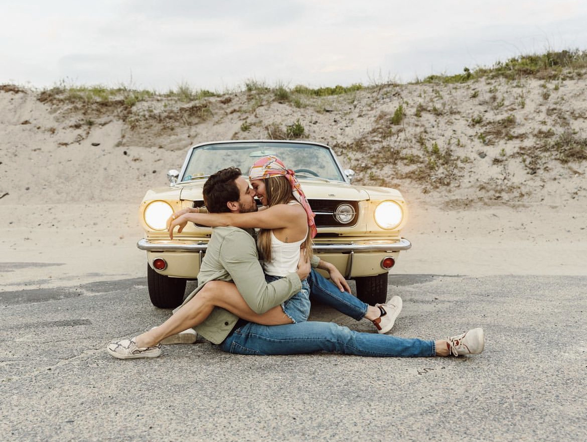Close-up of a pale yellow 1966 Ford Mustang convertible parked near the Newport coastline at sunset – classic car rental for weddings, photoshoots, and luxury experiences in Rhode Island.