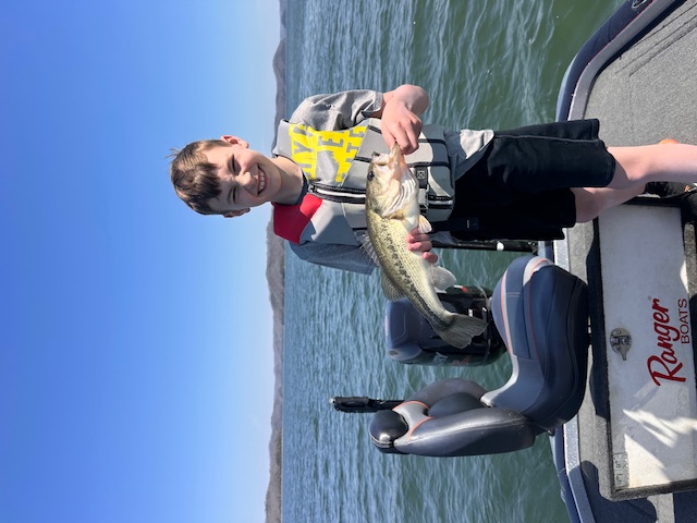 Child holding a bass fish on a boat