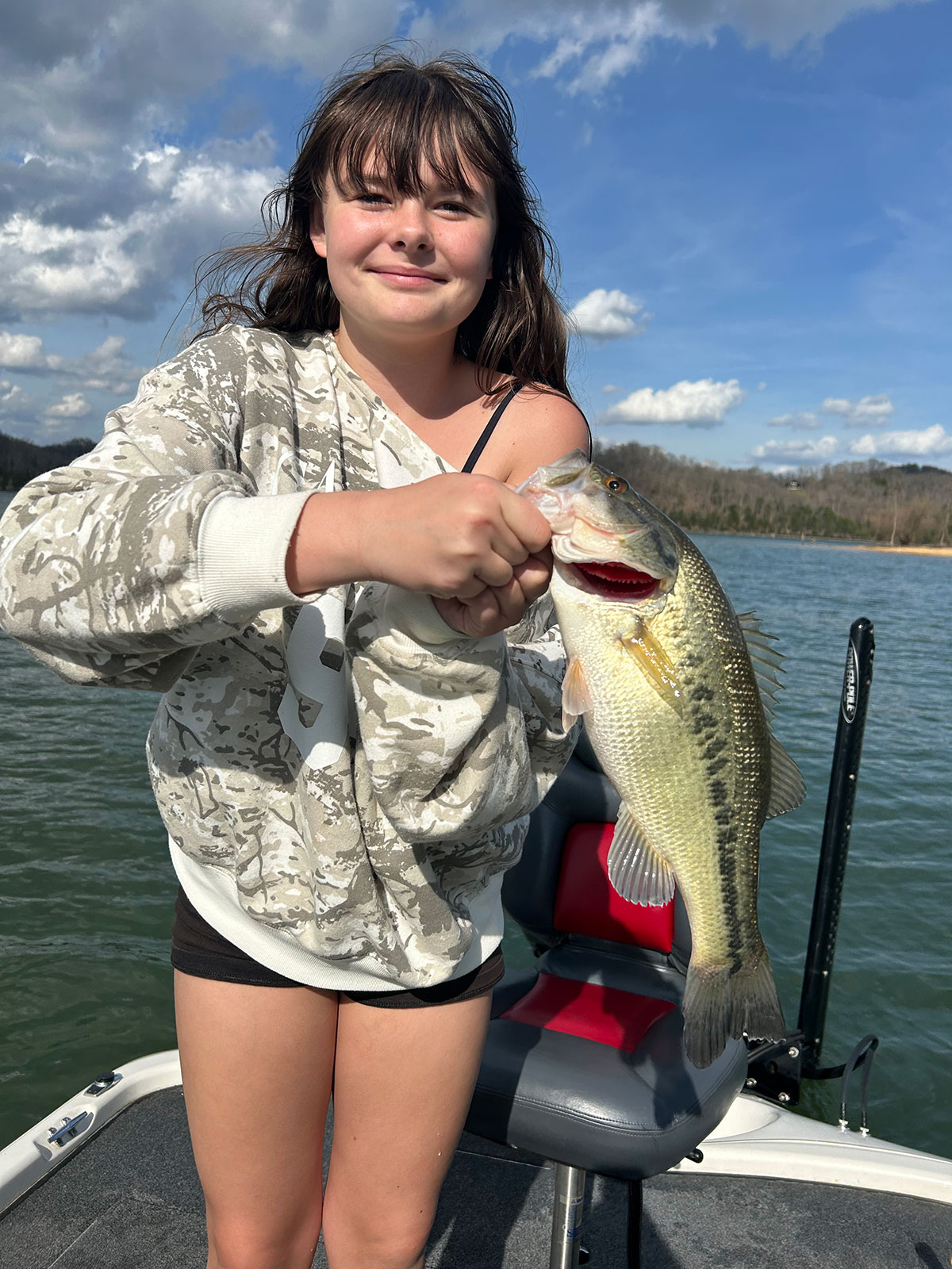 Child holding a bass fish on a boat