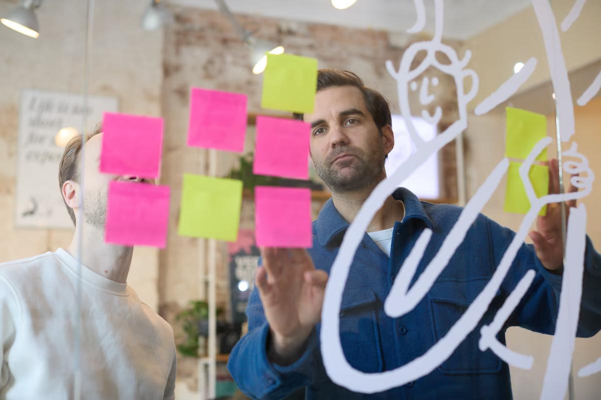 Twee teamleden van Evers + de Gier brainstormen bij een glazen wand vol post-its