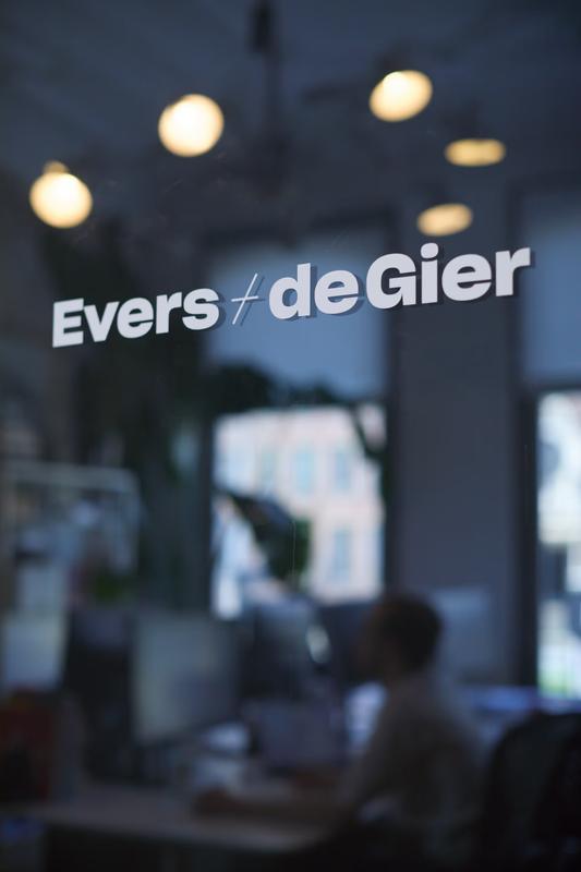 Het naambord 'Evers + de Gier' op het etalageraam van de studio met het interieur zichtbaar op de achtergrond