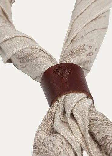 A natural cotton bandana rolled up and bound by a leather cuff printed with a California poppy