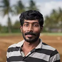 Man with short curly hair and beard wearing a black and white striped polo shirt outdoors.