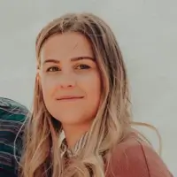 Close-up portrait of a smiling young woman with long blonde hair wearing a brown top.