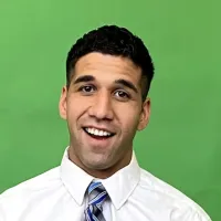Smiling man with short curly hair wearing a white shirt and striped tie on green background.