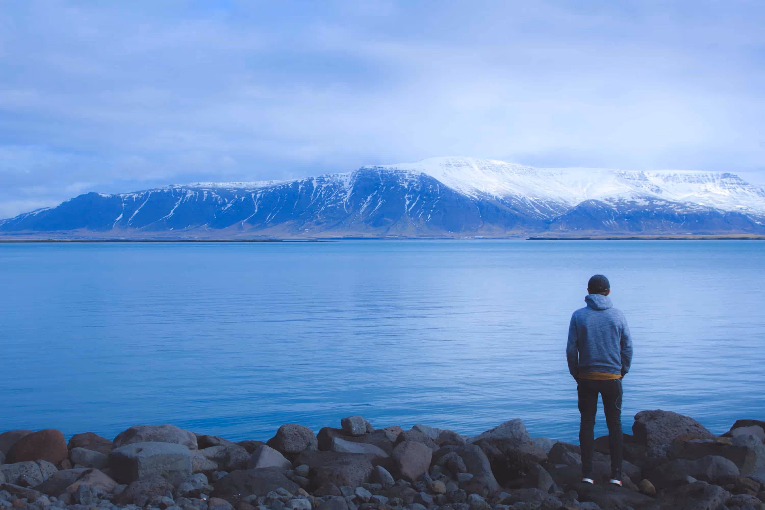 A man facing a mountain range with a lake in front.