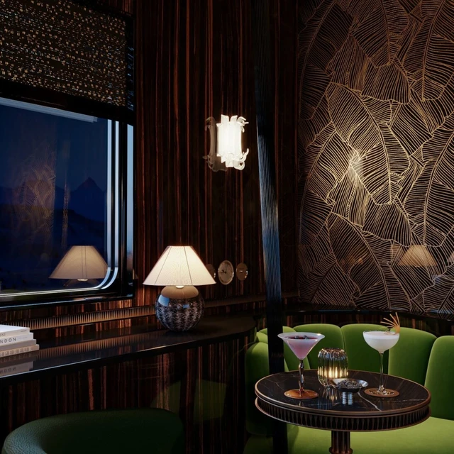 Moody shot of a table by the window during the evening in L'Orient Express' bar car, lighting provides a warm glow and artisinal cocktails sit on top of a table in front of rich-green seating.